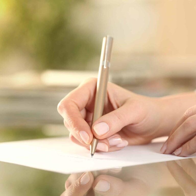 Woman hand writing on a paper on a desk at home